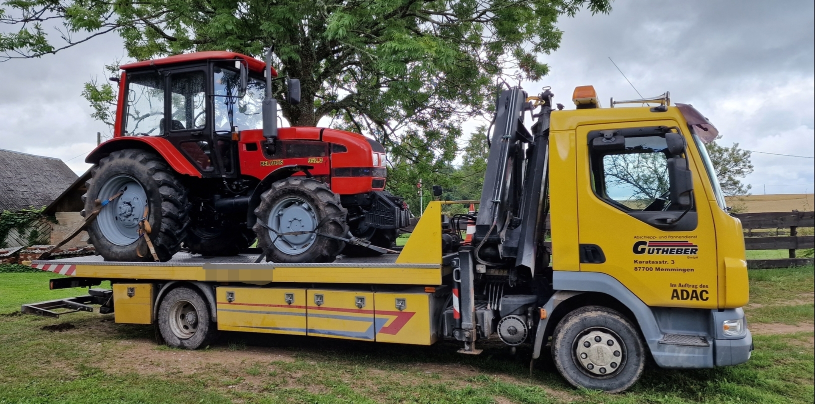 Evakuators, kas paceļ lielu traktoru no lauku teritorijas.
