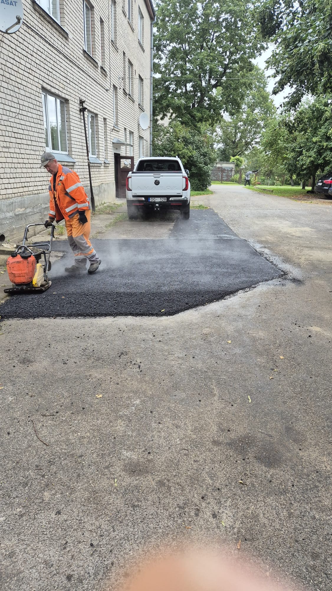 izmanto vibrācijas plāksni, lai sablīvēt uzklāto asfaltu būvniecības objektā.