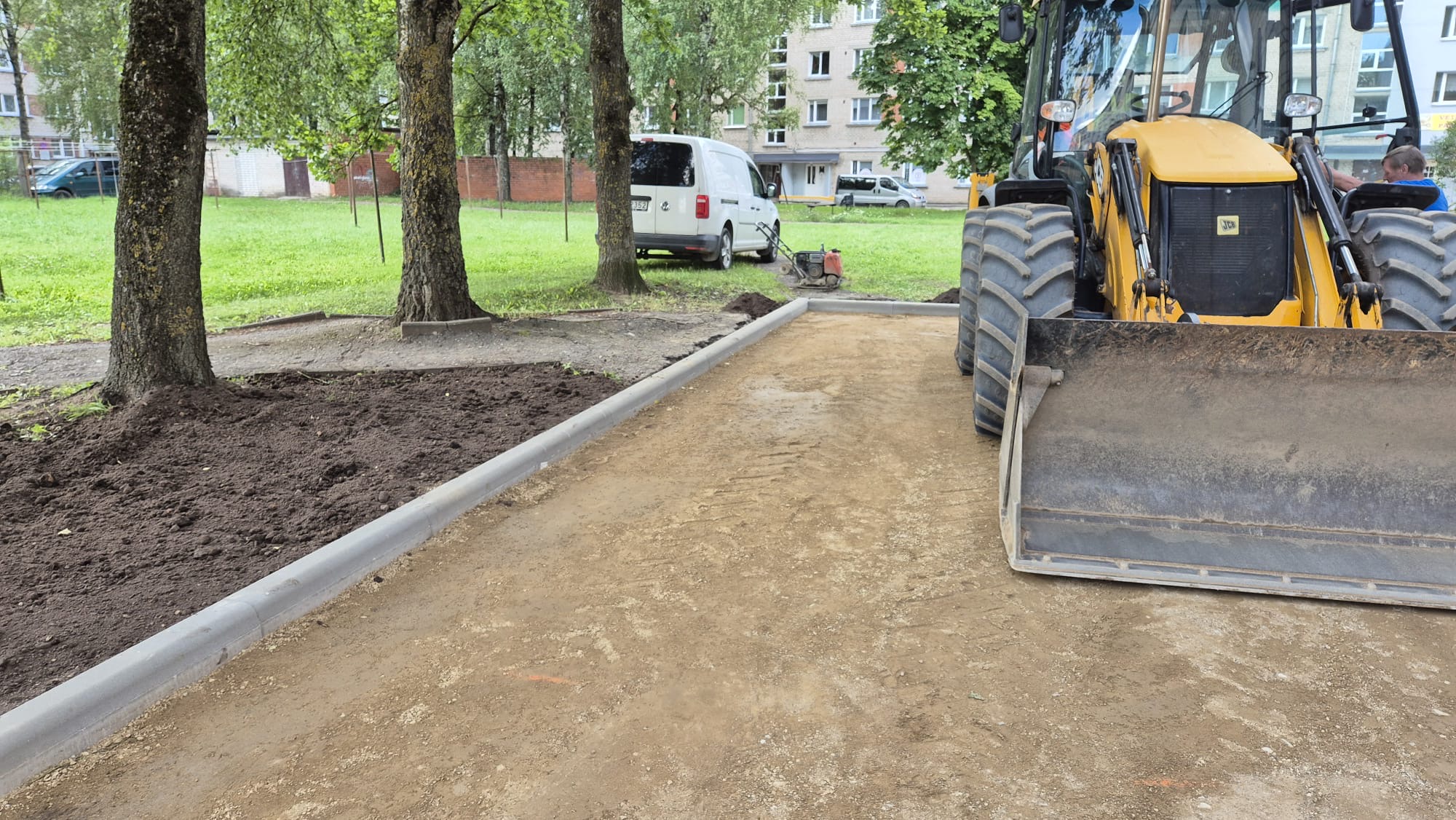 kskavators izlīdzina zemi ap jauniem ietves elementiem